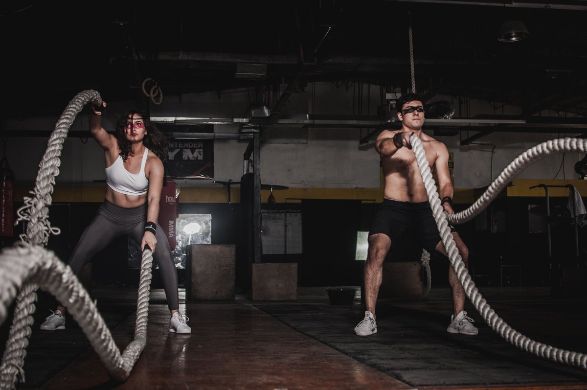Dos personas entrenando con cuerdas de batalla en un gimnasio.