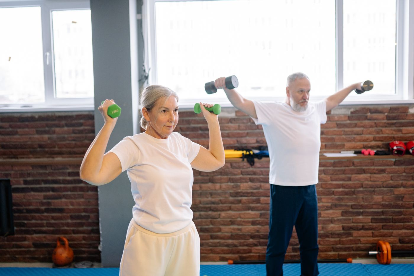 Pareja de personas mayores haciendo ejercicio con mancuernas en un gimnasio.